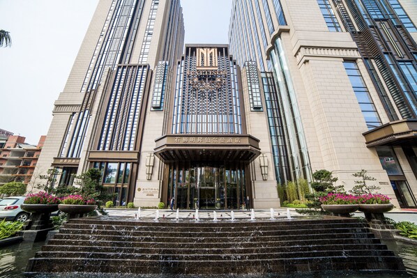 A modern hotel entrance with a grand staircase leading up to the doors, surrounded by water features and potted plants.