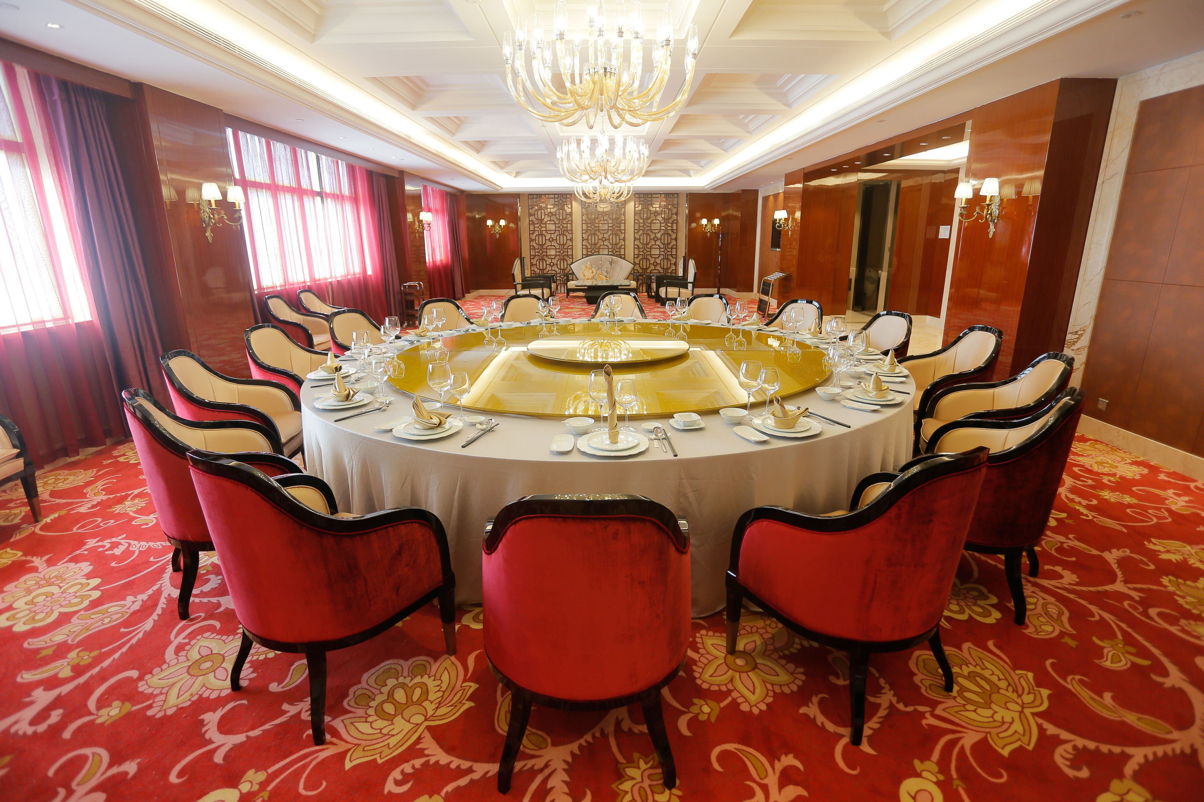 A formal dining room with a round table set for a meal, surrounded by red upholstered chairs.