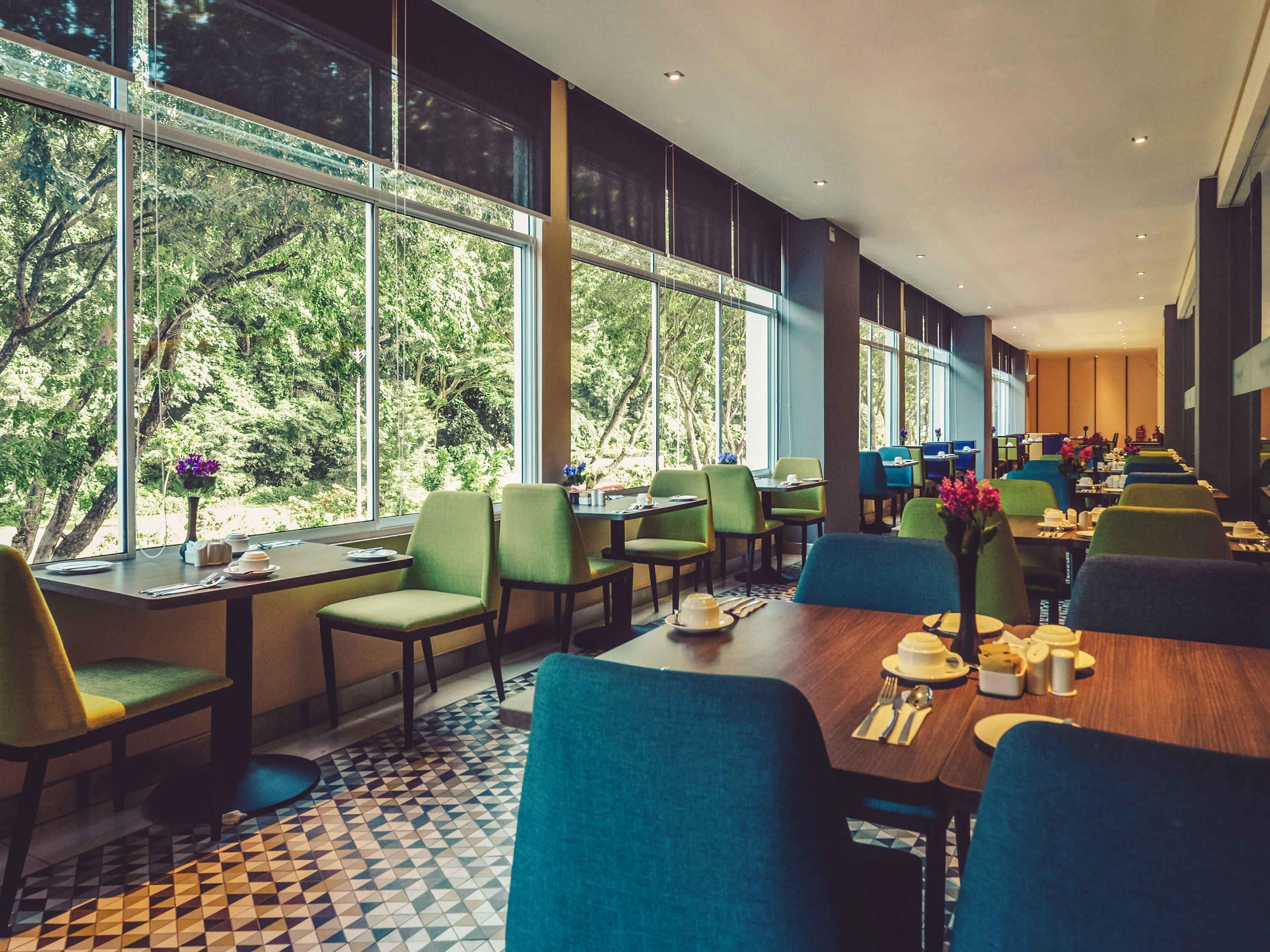 A modern dining area with large windows, green chairs, and a patterned floor.