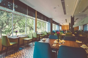 A modern dining area with large windows, green chairs, and neatly set tables.