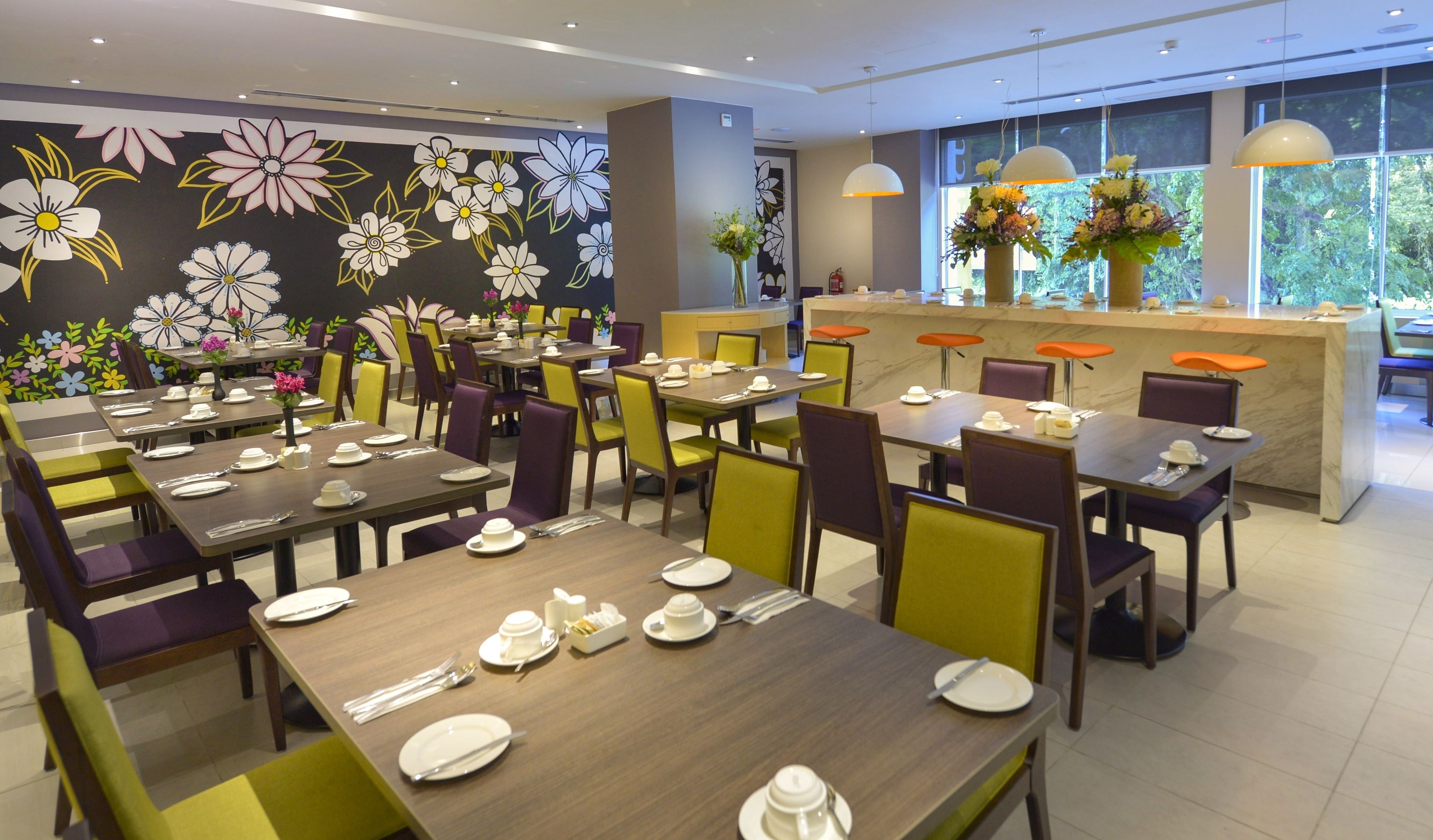 Un restaurant avec des tables dressées pour le service, un comptoir où est affiché le menu, et un mur décoré de motifs floraux.