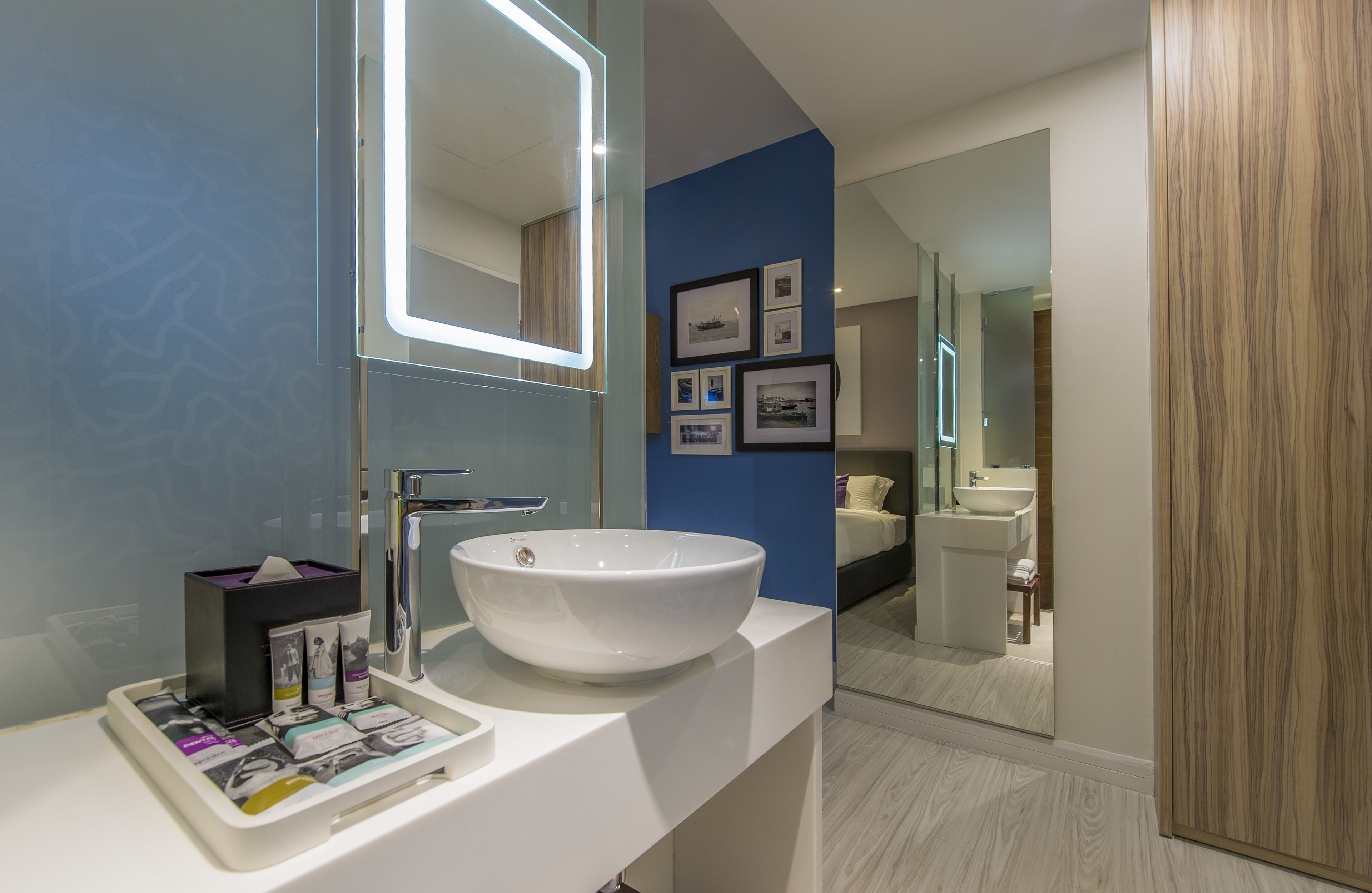 A modern bathroom with a large white sink, a mirror, and framed pictures on the wall.