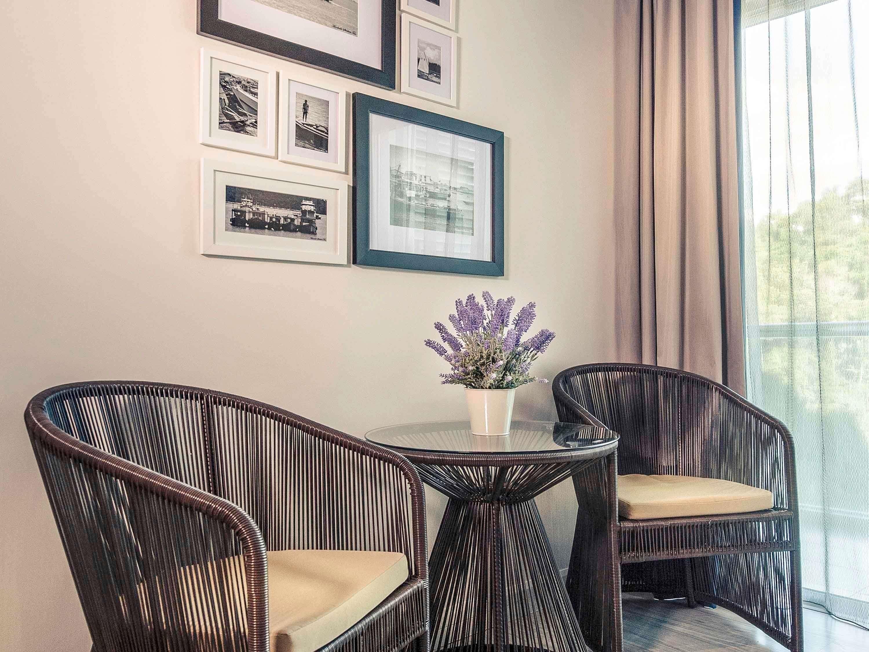 A room with a round table, two wicker chairs, a potted plant, and framed pictures on the wall.