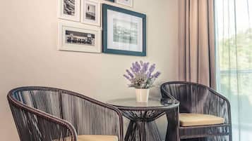 A room with a round table, two wicker chairs, a potted plant, and framed pictures on the wall.