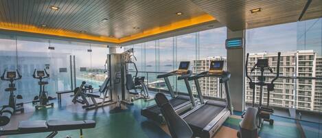 A gym with various exercise equipment, large windows, and a view of buildings.