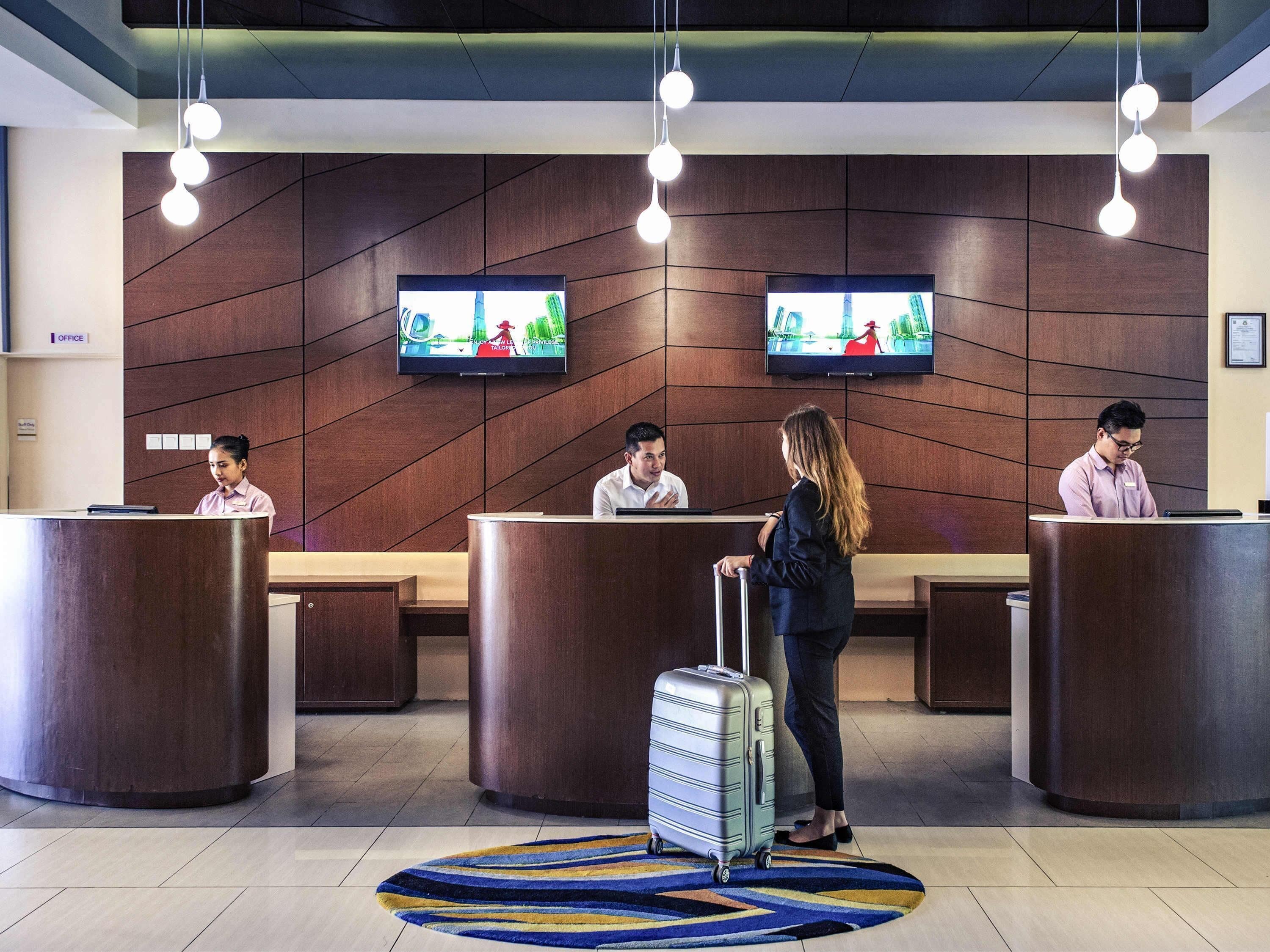 A hotel reception area with wooden reception desks, a large flat-screen TV, and a striped rug on the floor.