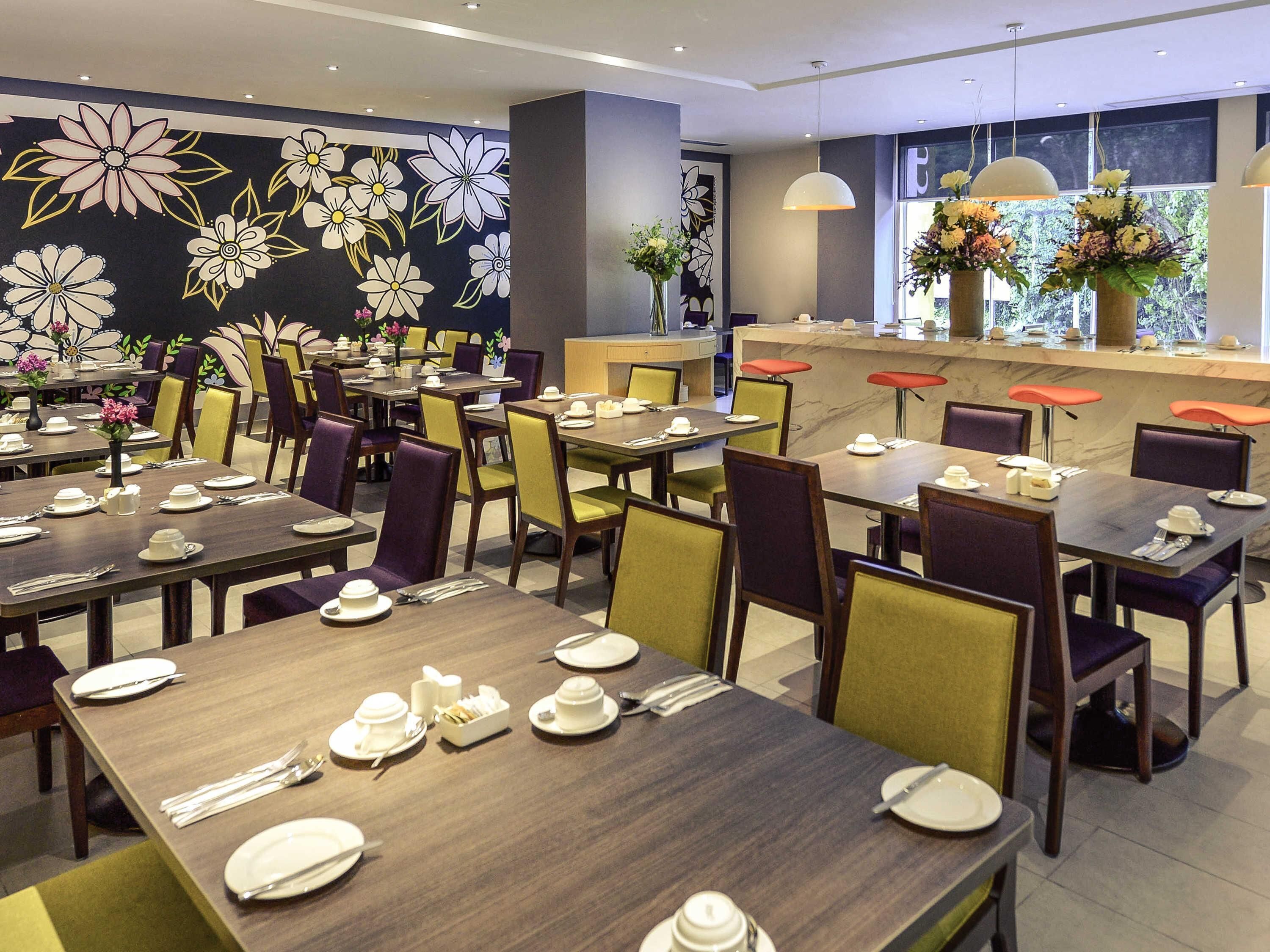 A restaurant with multiple tables set for dining, featuring a floral wall mural and a counter with a flower arrangement.