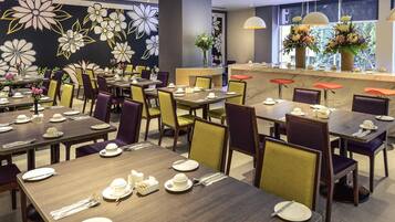 A restaurant with multiple tables set for dining, featuring a floral wall mural and a counter with a flower arrangement.