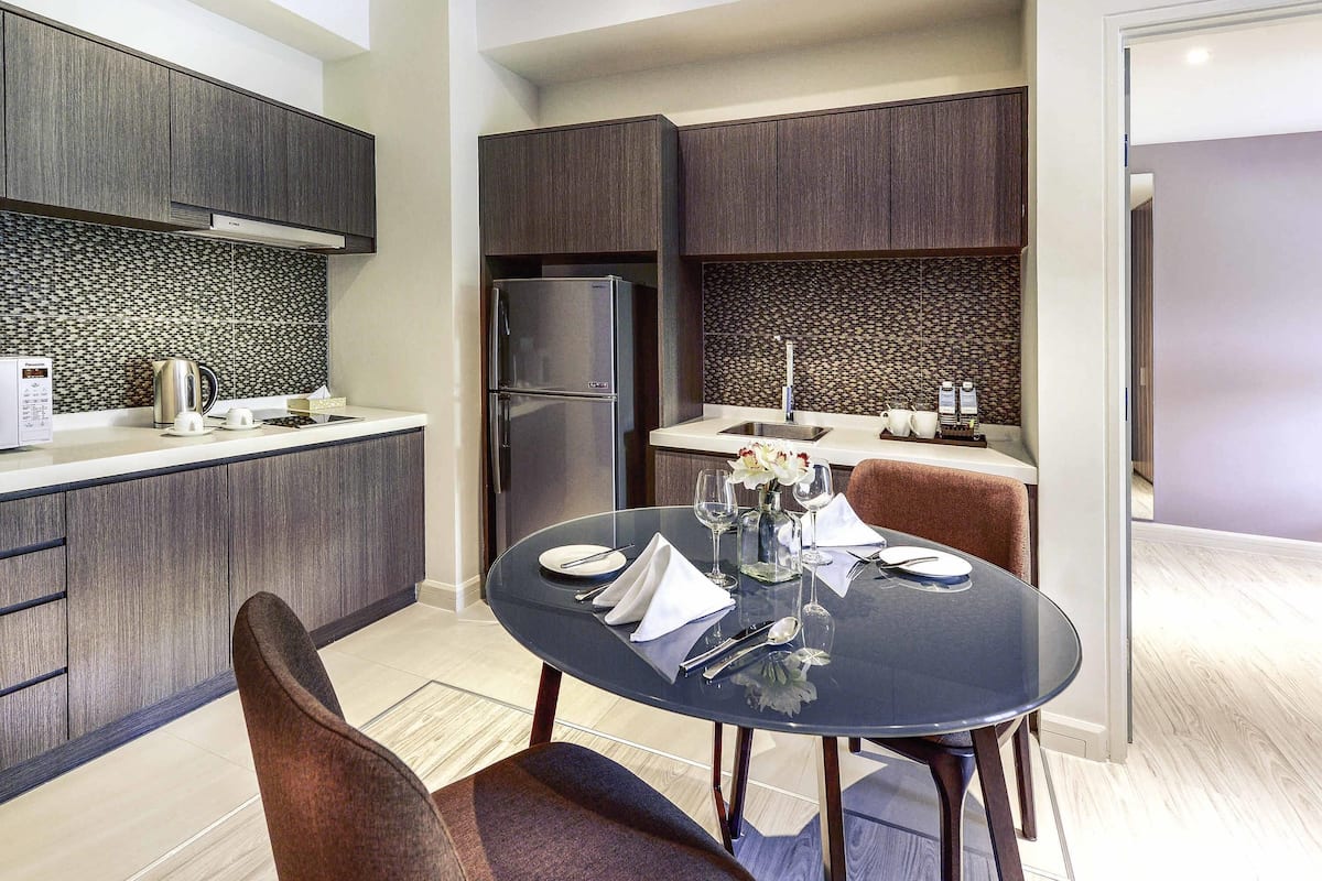A modern kitchen with dark wood cabinets, a stainless steel refrigerator, and a dining area with a round table and chairs.