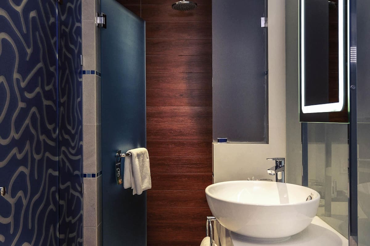 A modern bathroom with a large white sink, a wooden door, and a blue patterned wall.