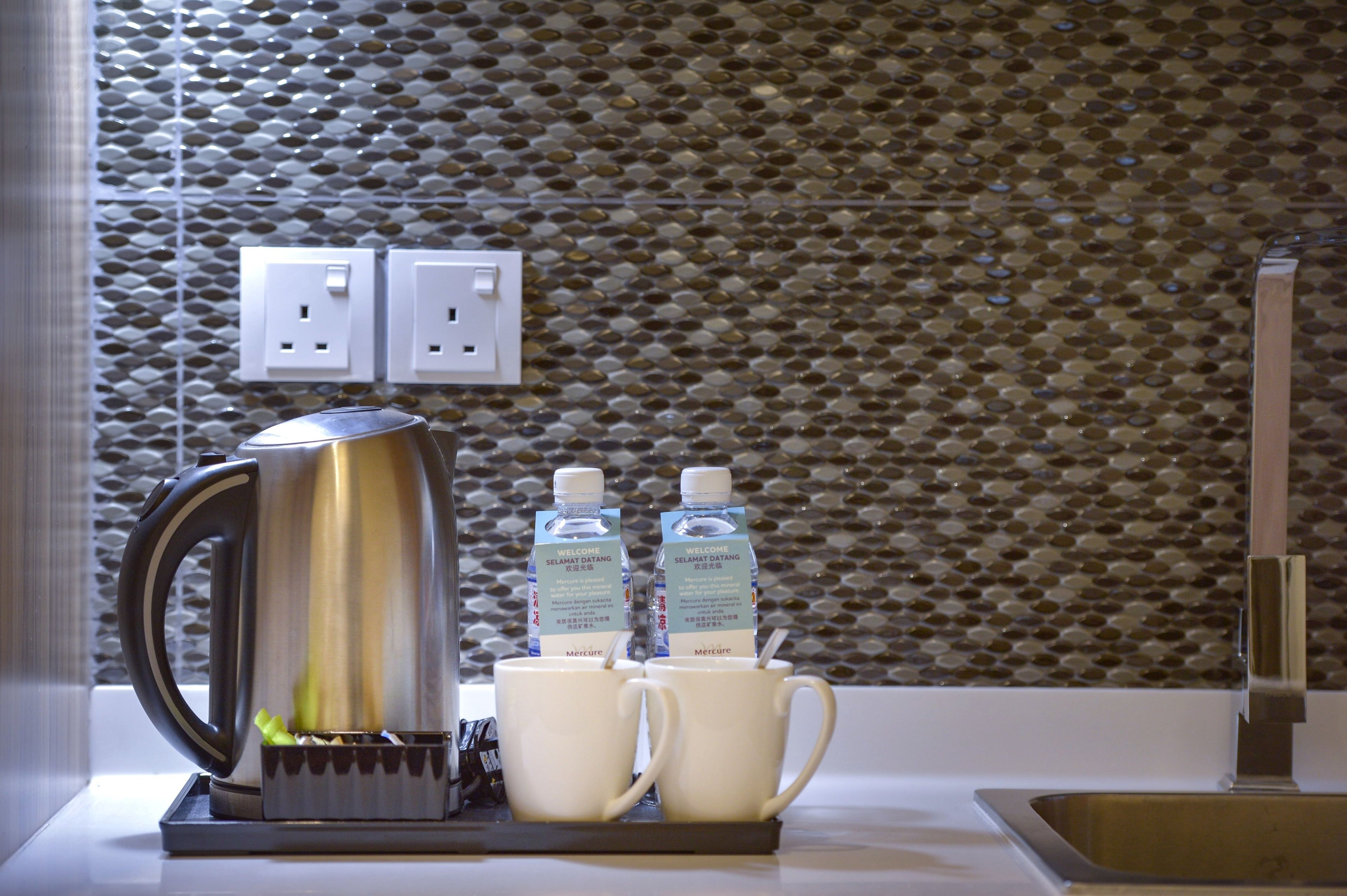 Una encimera de cocina con una tetera, dos tazas y dos botellas de agua.