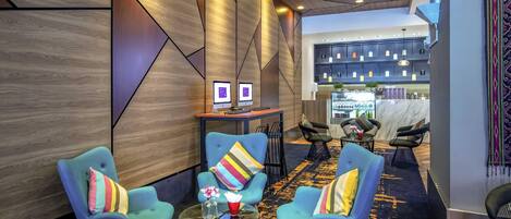 A modern lounge area with blue armchairs, a wooden table, and a bar area in the background.