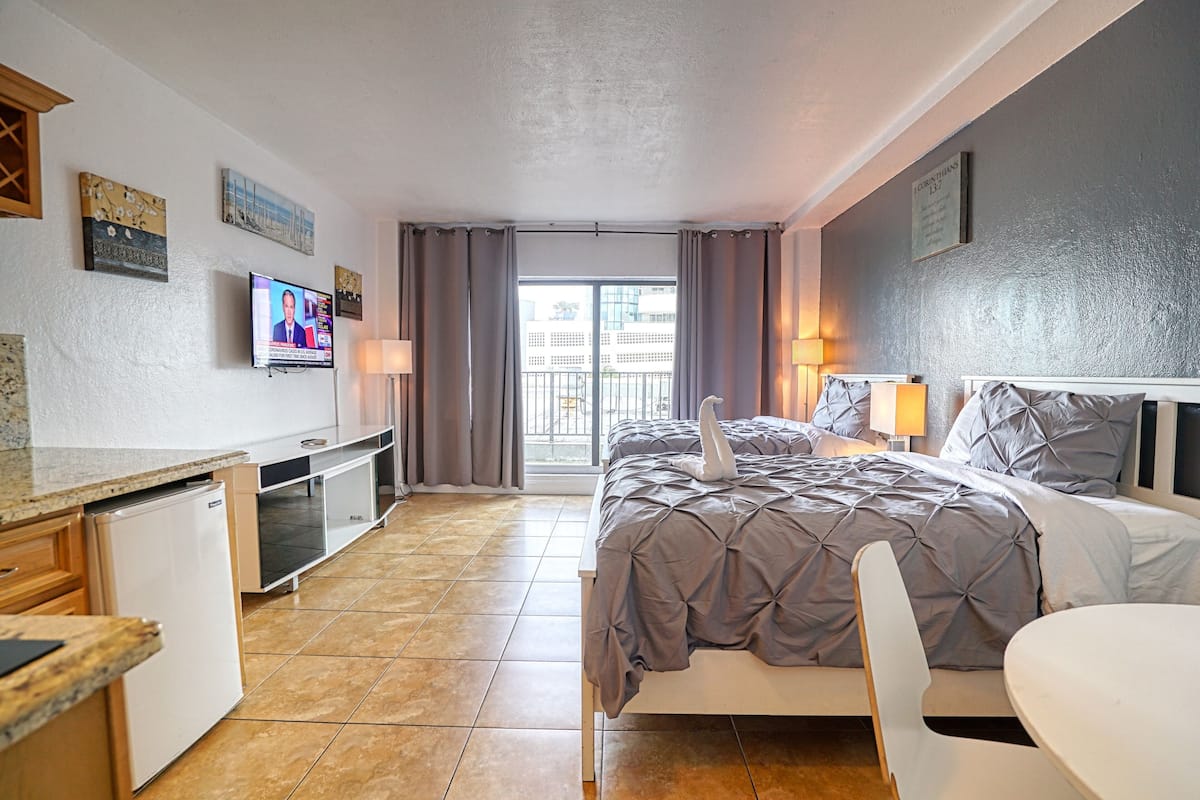 A hotel room with a bed, a desk, a TV, and a view of the outside.
