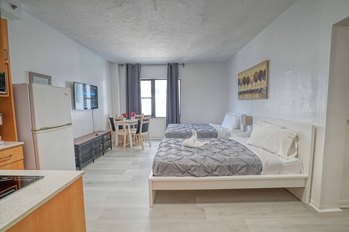 A compact hotel room with a bed, a desk, a chair, a refrigerator, and a television.
