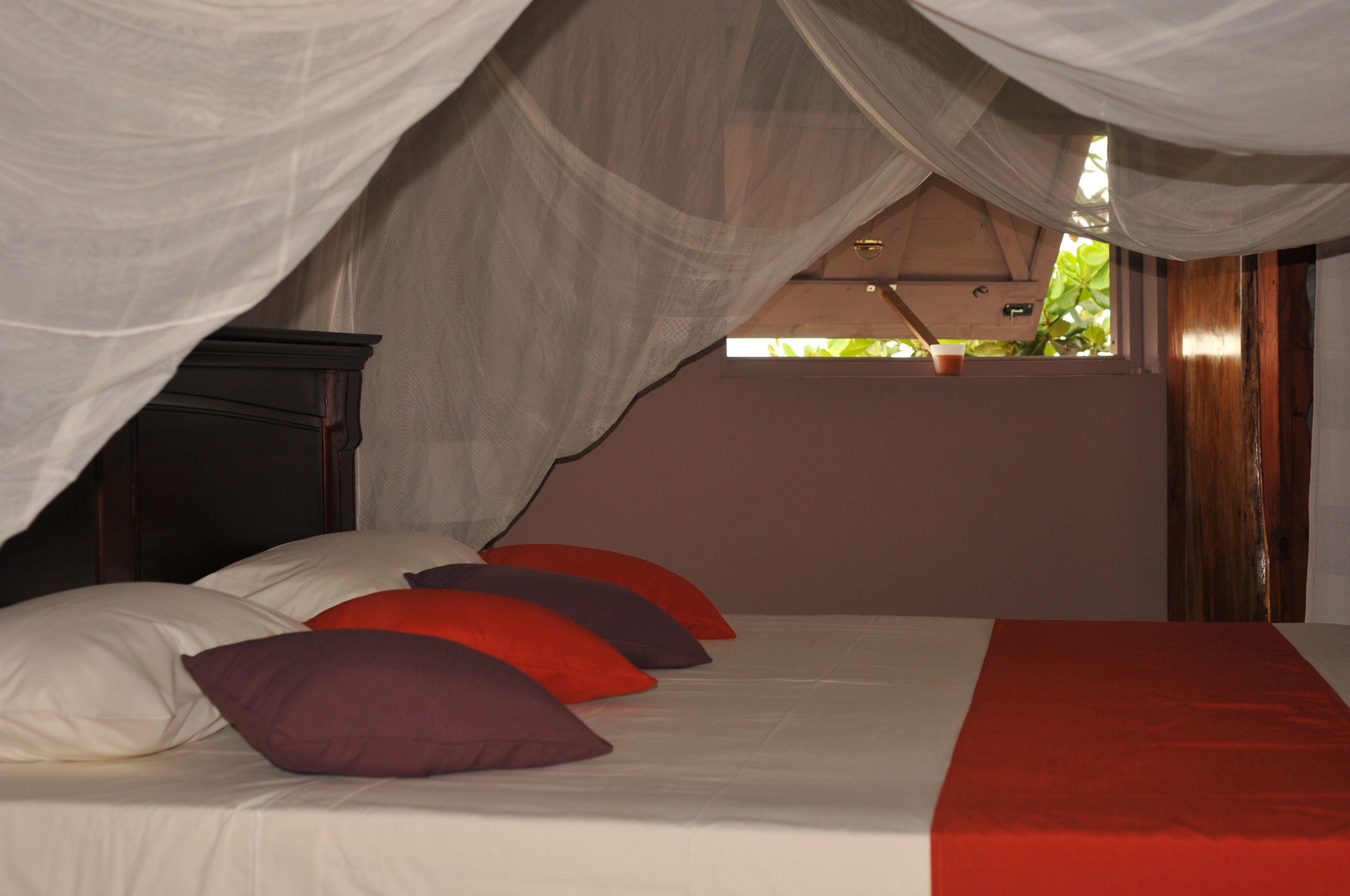 A bed with white and red bedding, a wooden headboard, and a canopy.