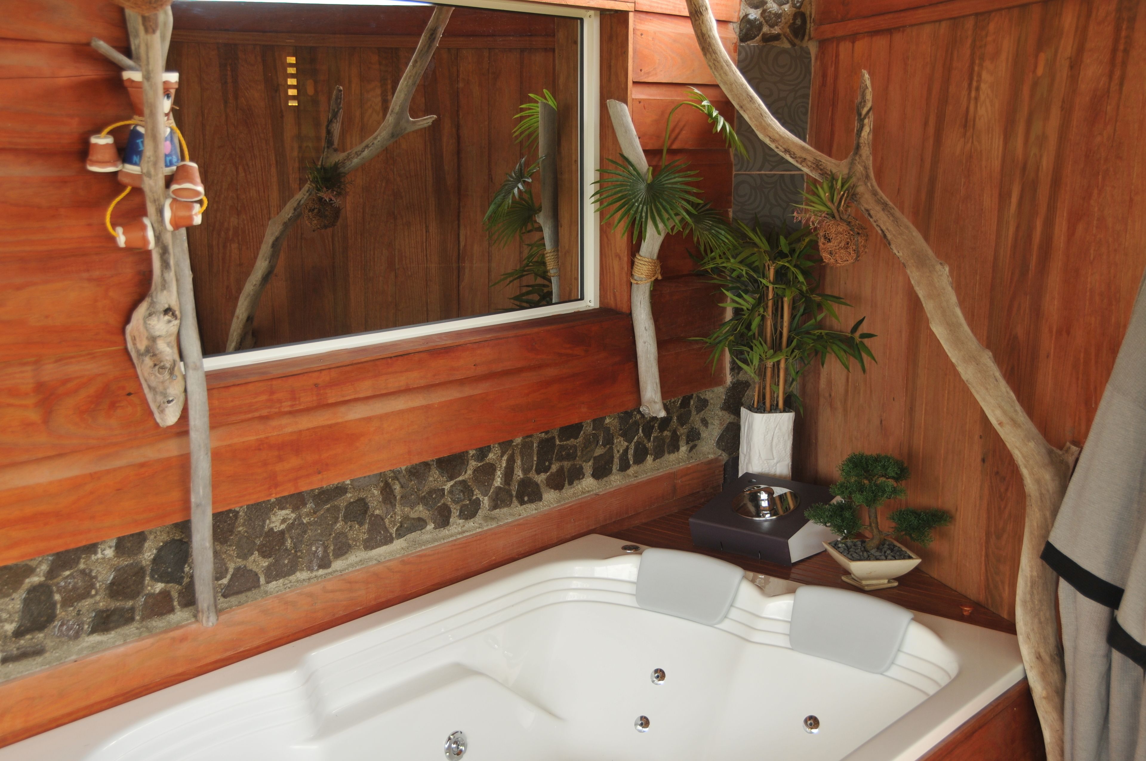 A bathroom with a wooden wall, a stone base, a large mirror, a bathtub, and a potted plant.