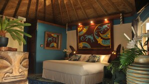 Een slaapkamer met een houten plafond, een bed met witte lakens, een blauwe muur en tropische decoratie.