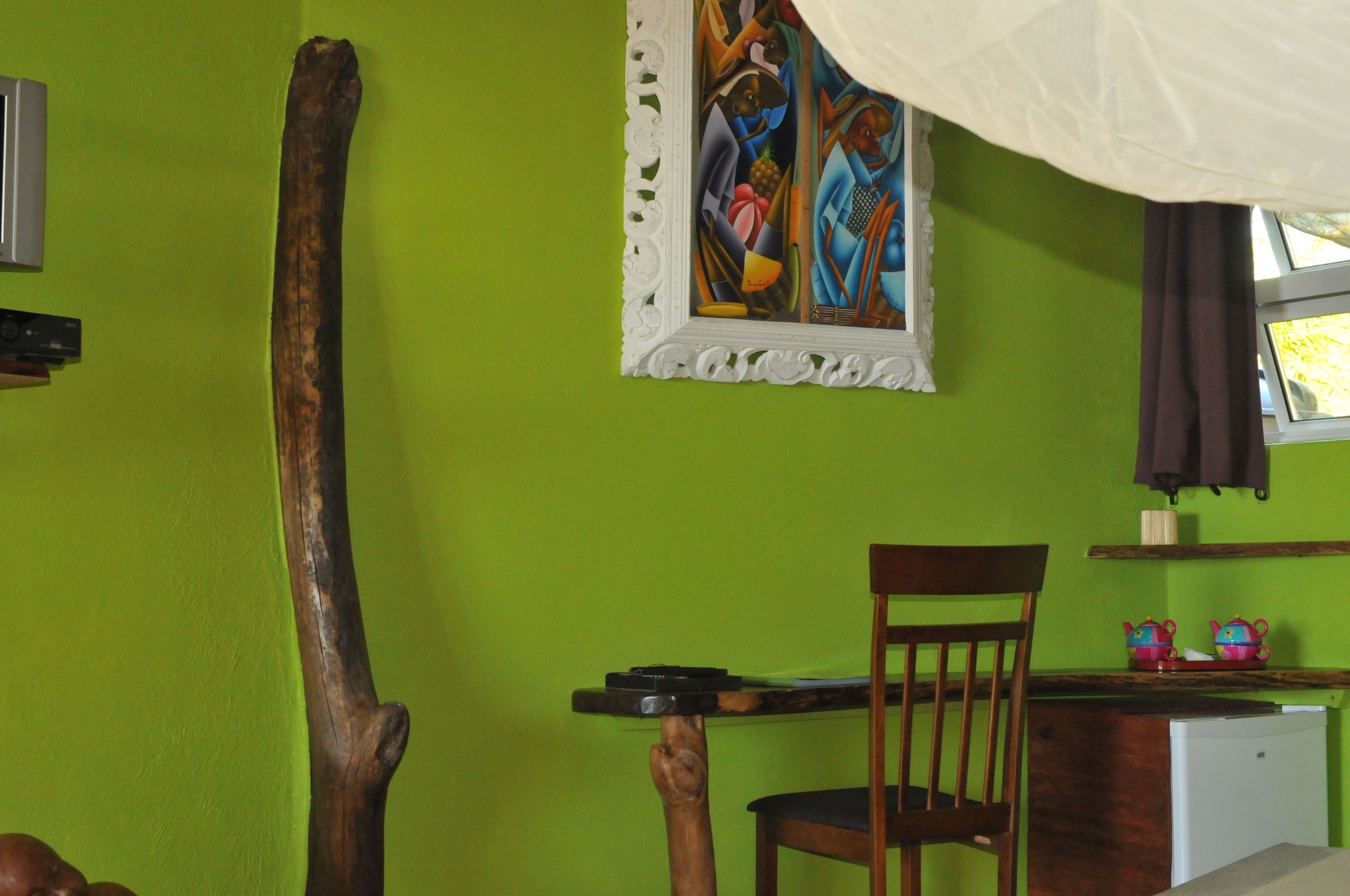 Una habitación con una pared verde, una silla de madera, una mesita pequeña, un armario blanco y un cuadro.