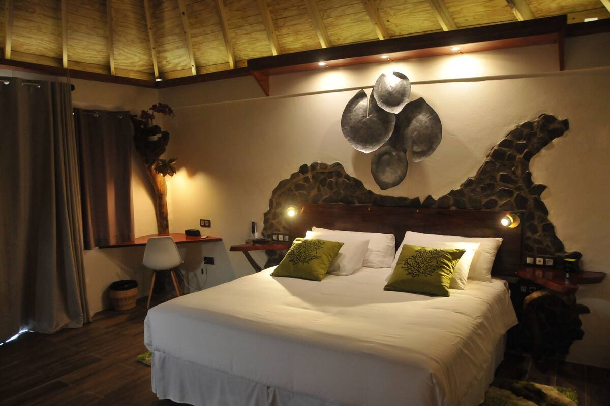 Un dormitorio con una cama grande, cabecera de madera, una escultura en la pared y un escritorio pequeño con una silla.