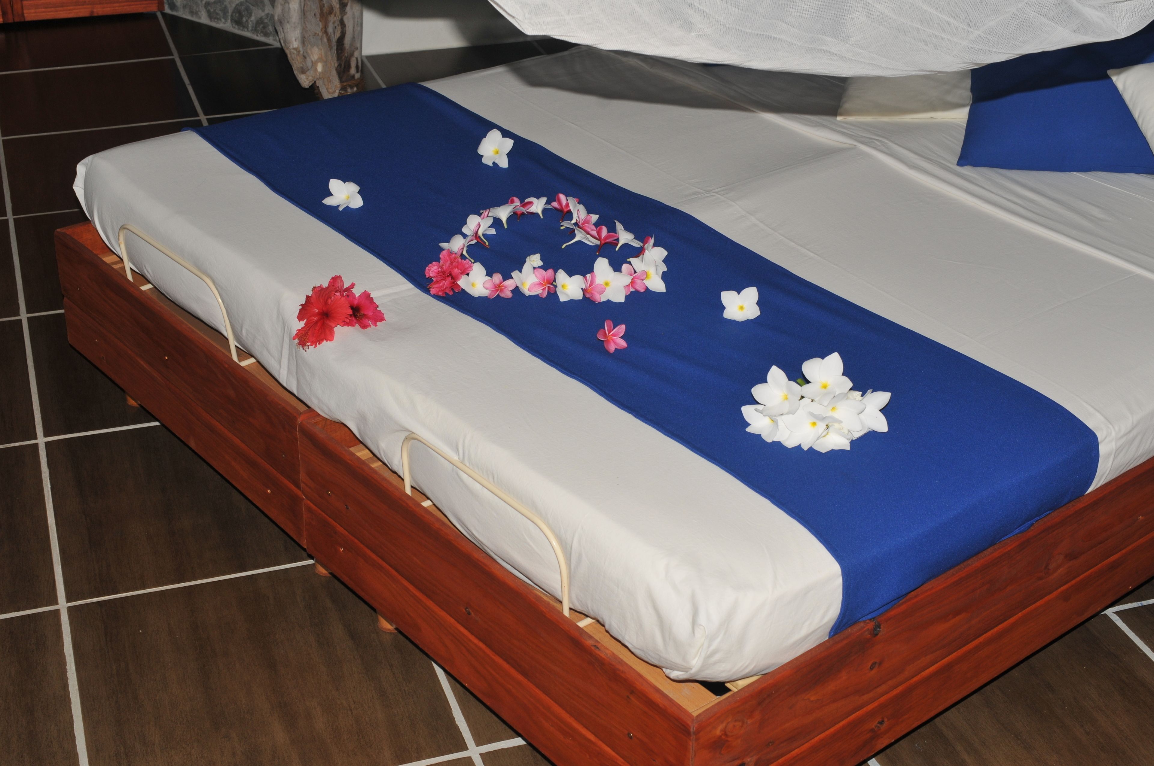 A bed with a blue and white bedspread, white pillows, and a floral arrangement on the bed.