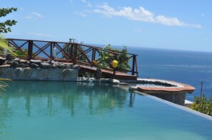 Una piscina infinita con terraza y barandilla de madera con vistas al océano.
