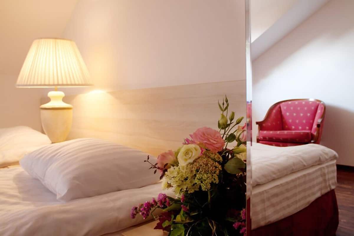 Una habitación de hotel con una cama, una lámpara de noche, un arreglo floral y una silla roja.