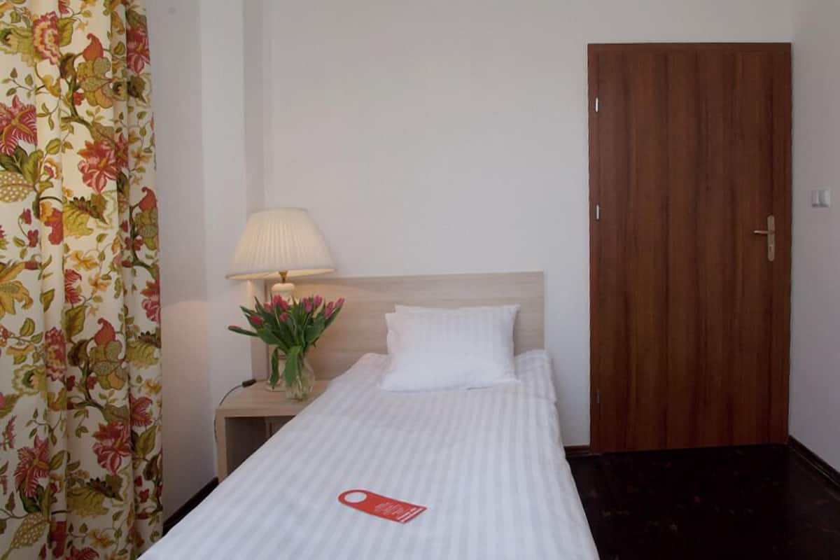 Una habitación de hotel con cama, mesita de noche, lámpara, puerta y cortinas con estampado floral.