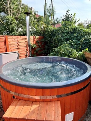 A hot tub with a wooden exterior, surrounded by a wooden deck and a metal heater. - Kuźnia Pałacowa (Korczew)