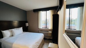 Een hotelkamer met een groot bed, een nachtkastje met een lamp, een raam met gordijnen en uitzicht op de stad.