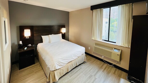 Een hotelkamer met een groot bed, bedlampjes, een nachtkastje, een raam met gordijnen en een wandradiator.