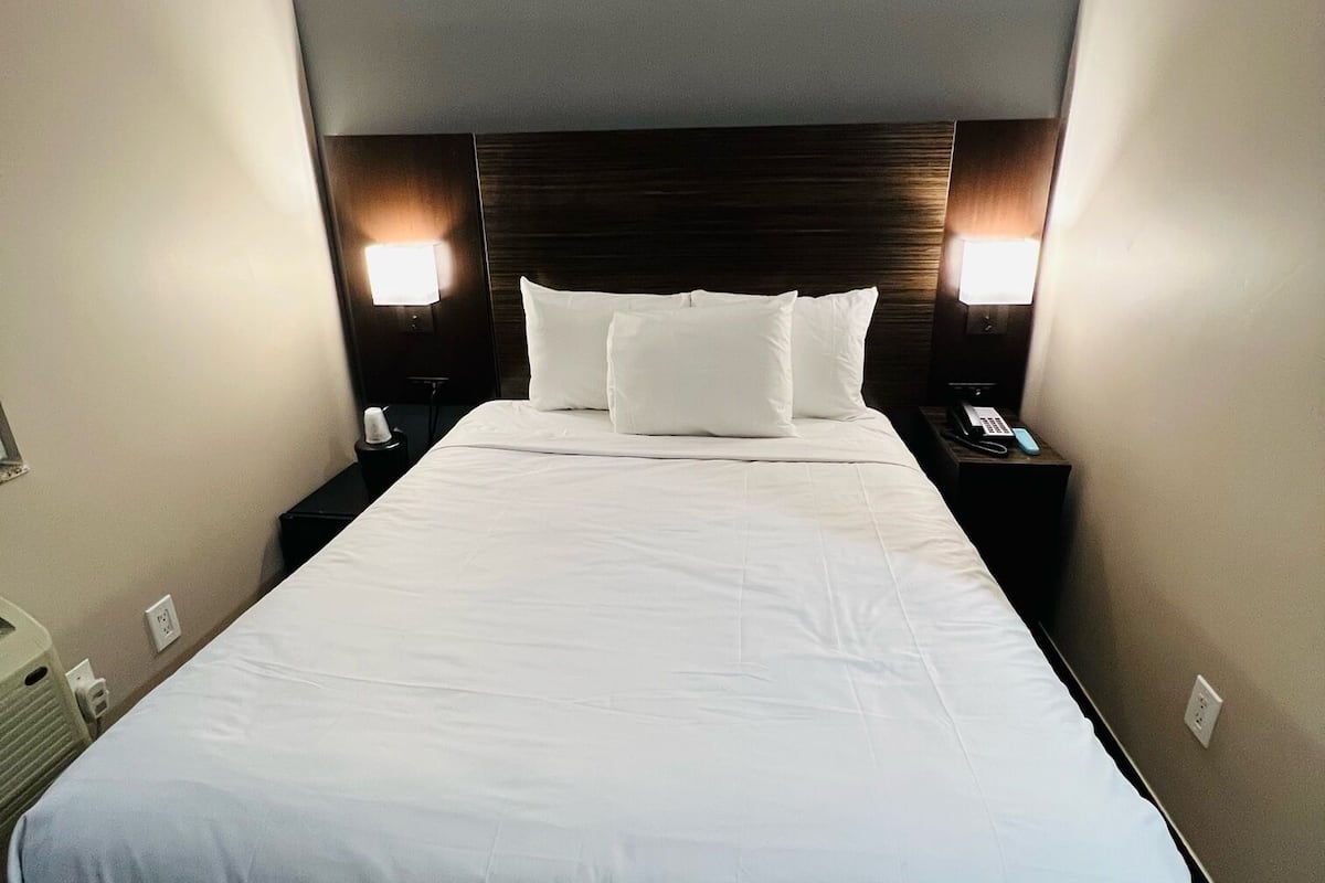A hotel room with a large bed, two bedside lamps, and a dark headboard.