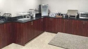 Een keuken met houten kastjes, een aanrecht en diverse apparaten, waaronder een koelkast, magnetron en broodrooster.