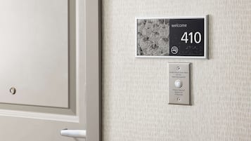 Una porta con un cartello di benvenuto e il numero '410', che indica la stanza. Sotto il cartello, un sistema di avviso audiovisivo per persone con problemi di udito, con un pulsante da premere per 5 secondi.