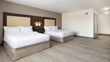 A hotel room with two beds, a wooden headboard, a nightstand, a refrigerator, and a carpeted floor.
