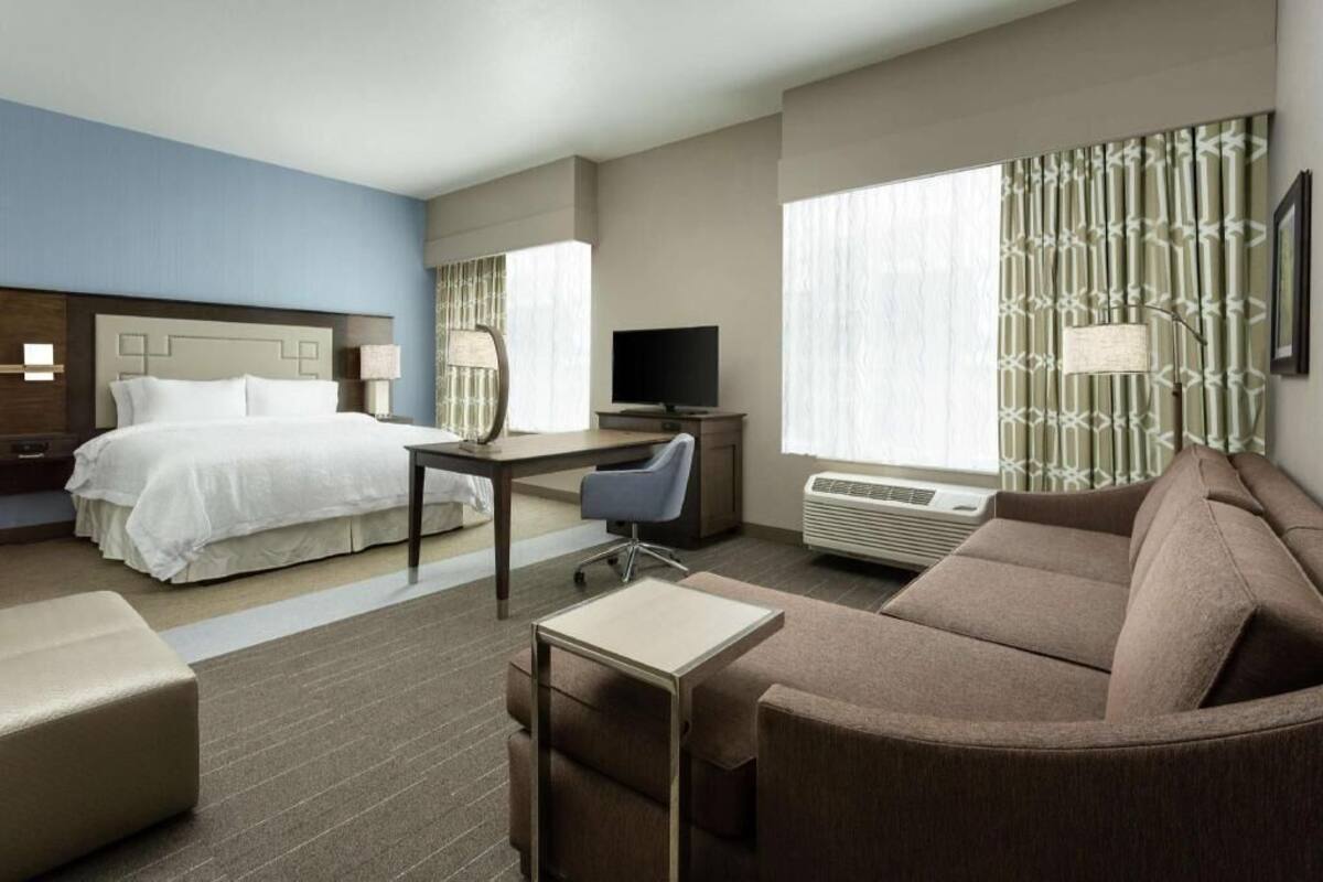 A hotel room with a bed, desk, chair, couch, and a television.