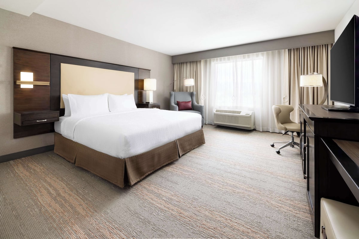 A hotel room with a large bed, a desk with a chair, a TV, and a window with curtains.