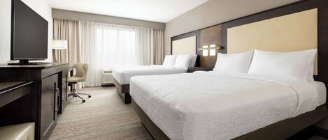 A hotel room with two beds, a desk with a flat-screen TV, a chair, and a lamp.