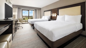 A hotel room with two beds, a desk, a chair, and a TV.