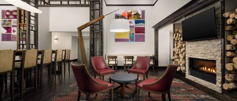 A modern lounge area with a fireplace, a round table with chairs, and a large TV screen.