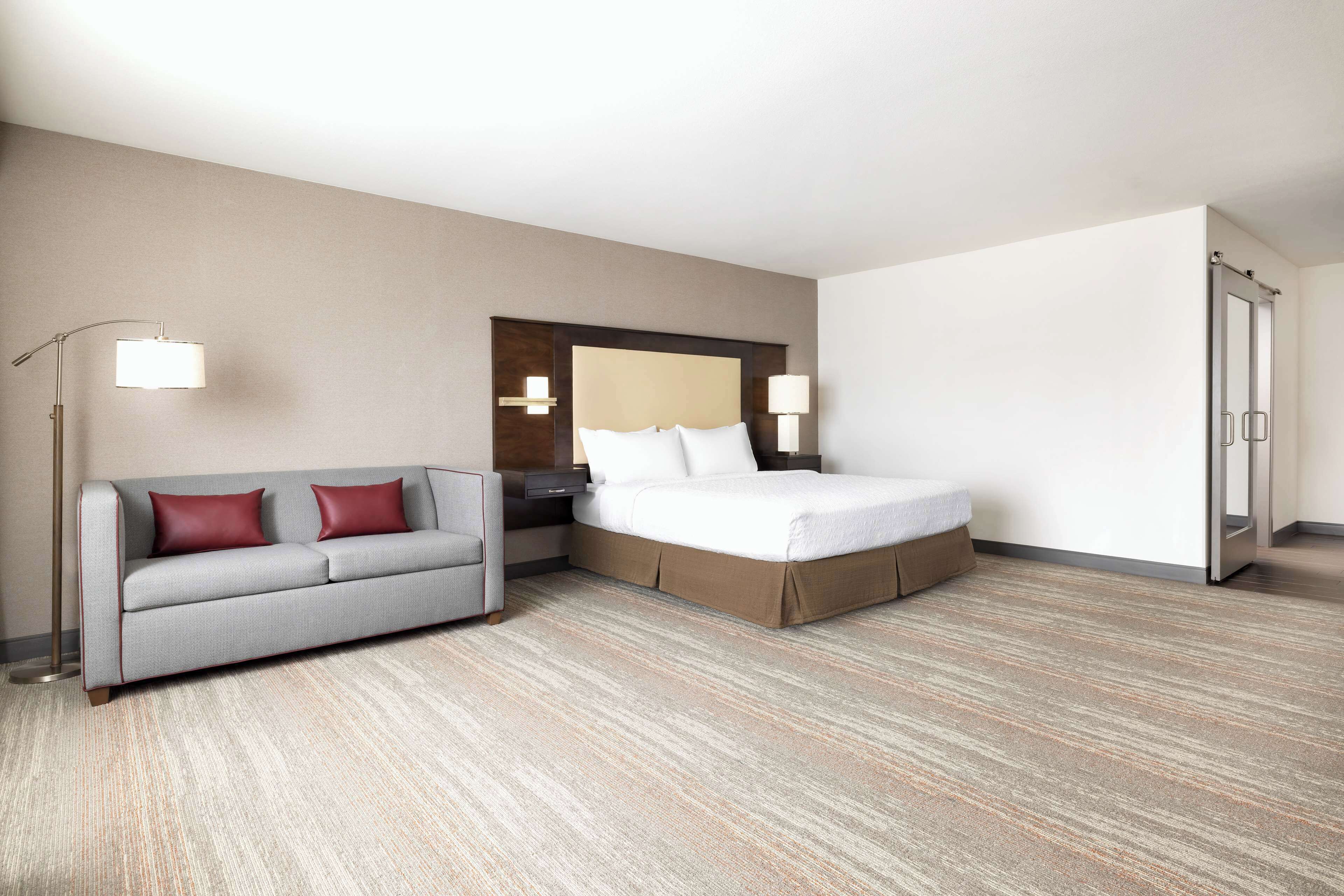 Una habitación de hotel con cama, sofá, mesita de noche, lámpara y armario.