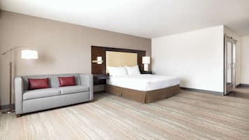 Una habitación de hotel con cama, sofá, mesita de noche, lámpara y armario.