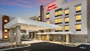 A modern hotel with a stone facade, a covered entrance, and a sign reading "Hampton Inn & Suites".