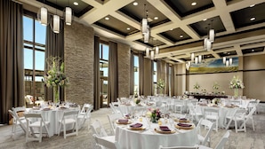 A banquet hall with round tables set for dining, white chairs, and large windows allowing natural light.