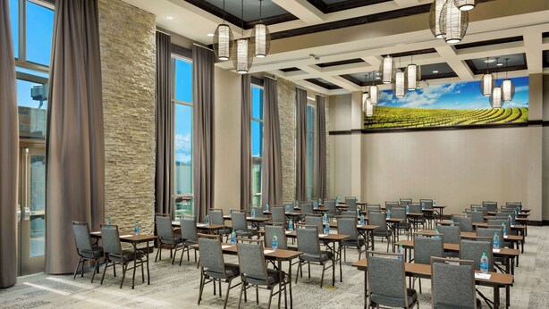 A conference room with rows of tables and chairs, large windows, and a stone accent wall.