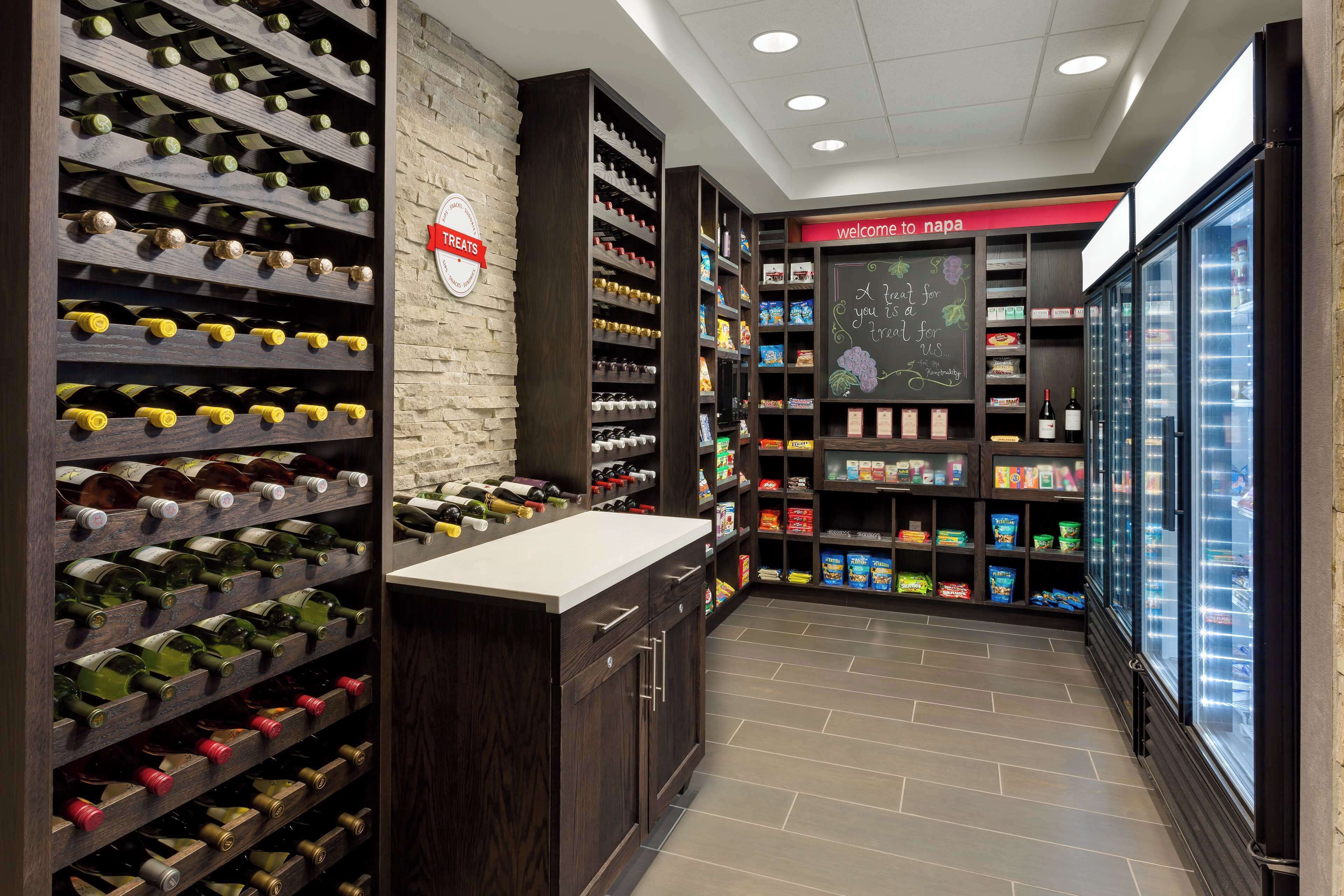 A wine cellar with shelves of wine bottles, a chalkboard with a welcome message, and a refrigerated display case.