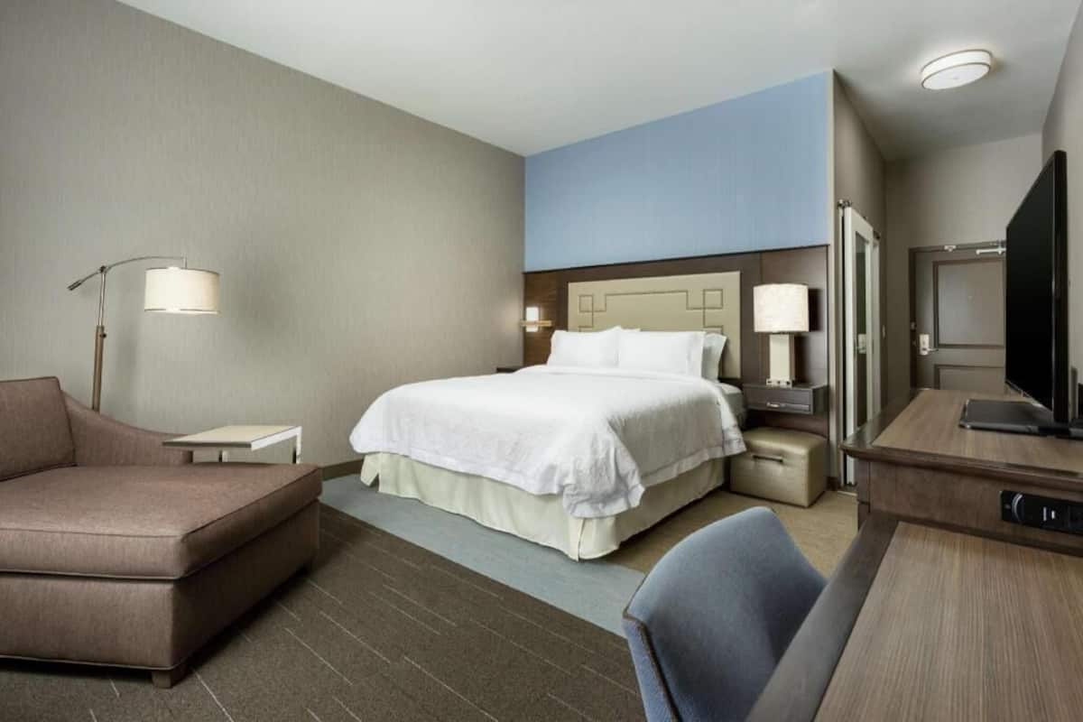 A hotel room with a bed, a desk, a chair, a lamp, and a television.