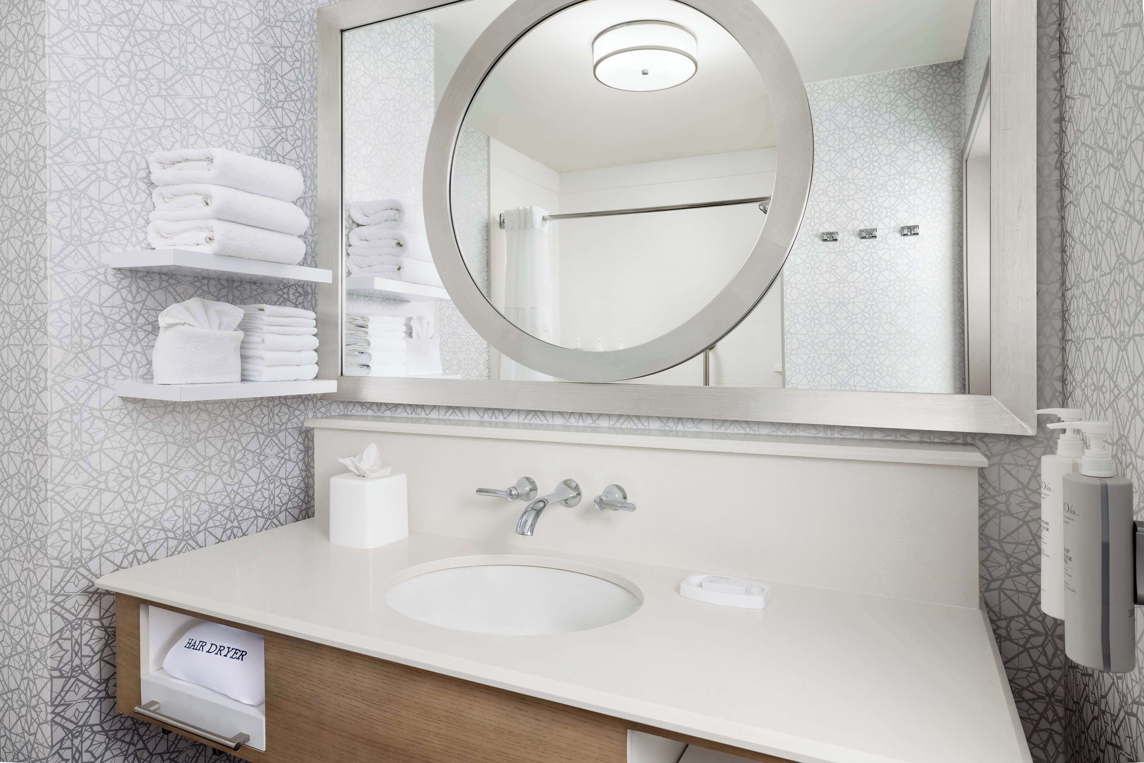 A bathroom with a round mirror, a sink, and a towel rack with folded towels.