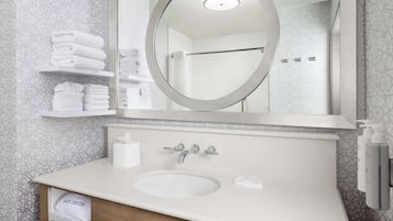 A bathroom with a round mirror, a sink, and a towel rack with folded towels.