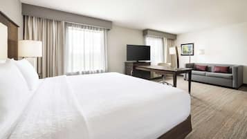 A hotel room with a large bed, a desk with a flat-screen TV, a sofa, and a window with curtains.