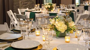 A banquet table set with white plates, gold cutlery, and clear glassware, adorned with candles and a floral centerpiece.